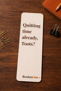 Bookmark with text 'Quitting time already, Toots?' on a wooden surface with stationery items.