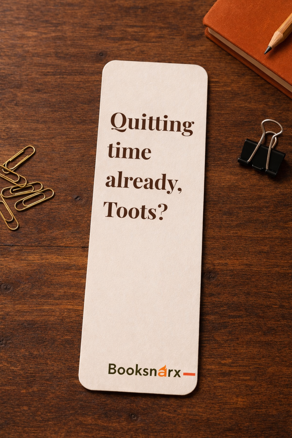 Bookmark with text 'Quitting time already, Toots?' on a wooden surface with stationery items.