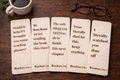 Five wooden bookmarks with humorous text on a wooden surface with a cup of coffee and glasses.
